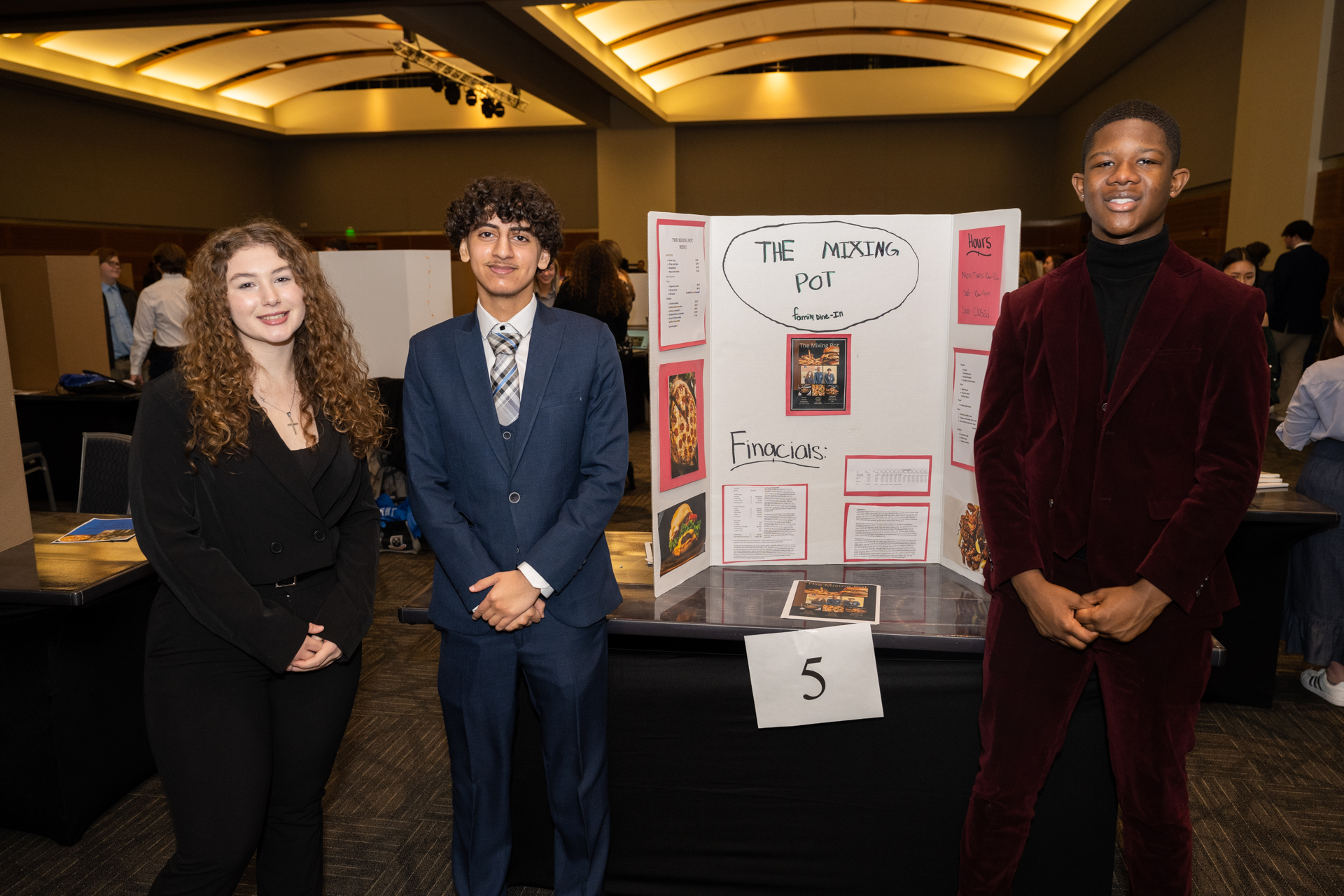3 highschool students stand in front of a poster describing their business. The poster reads, "The Mixing Pot".