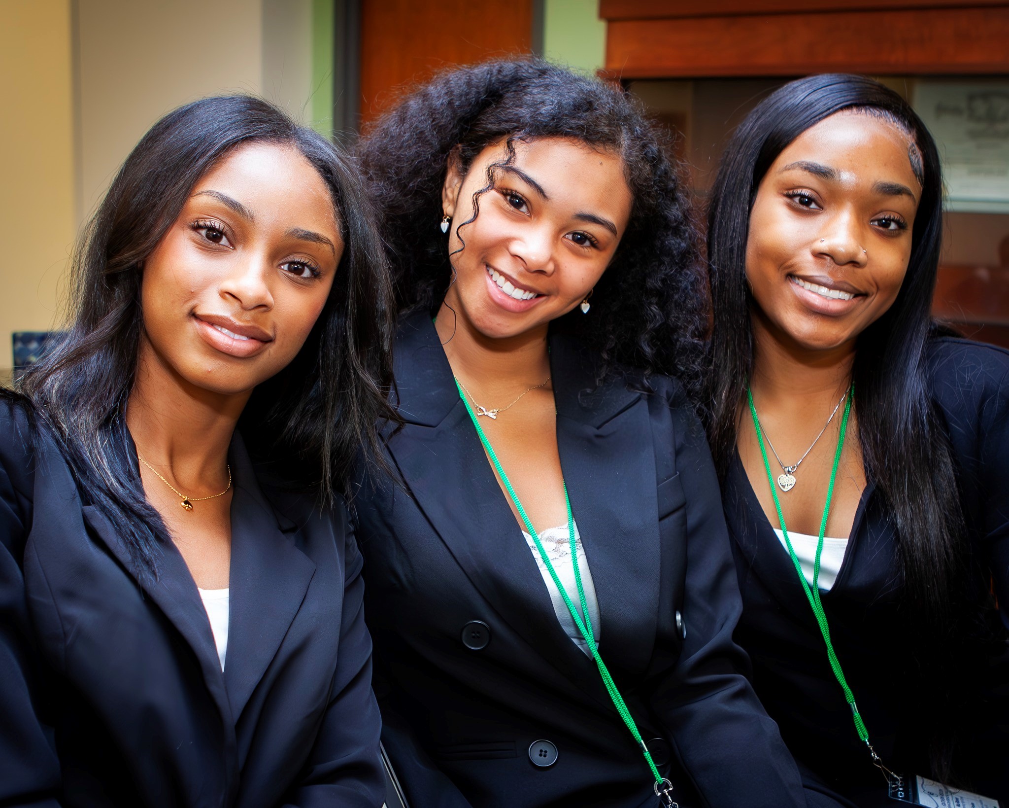 Three female students wearing blazers smile for the photo