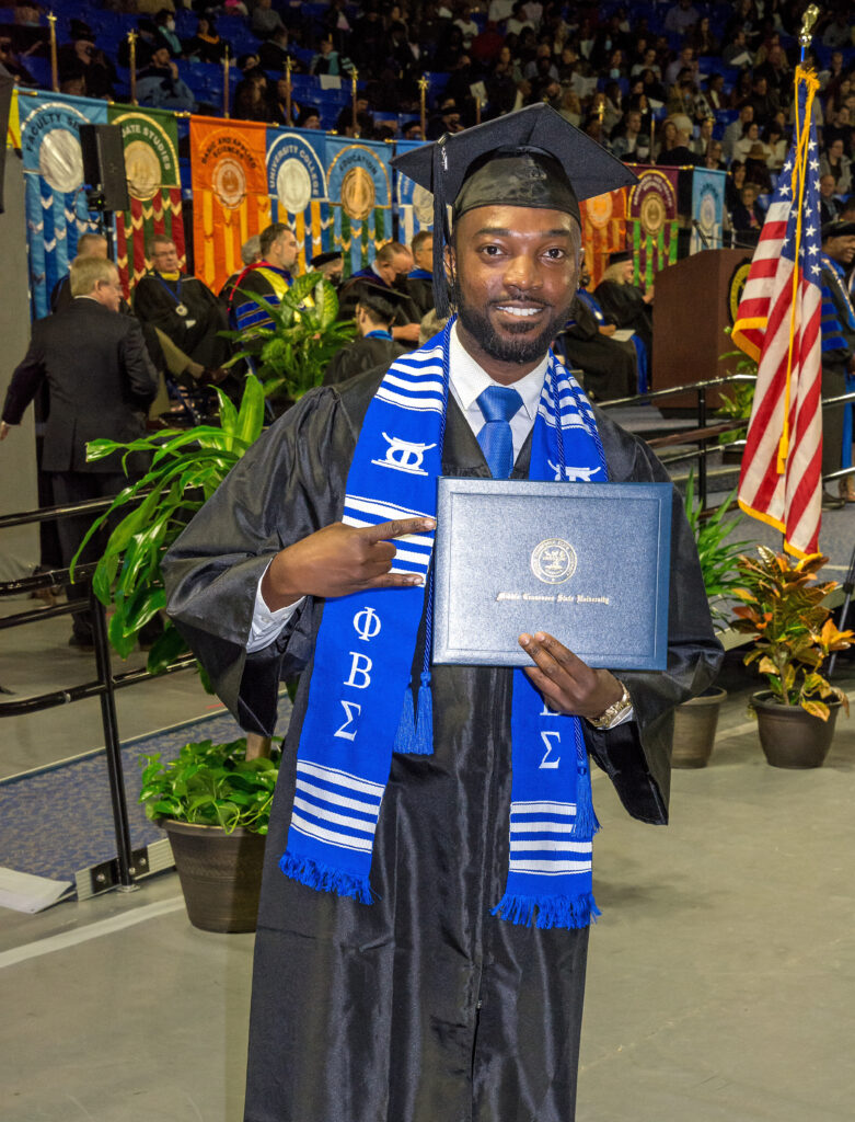 man poses with mtsu degree at a commencement ceremony
