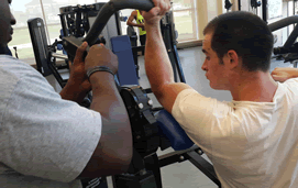 Photo of a trainer helping his client with a machine bicep curl